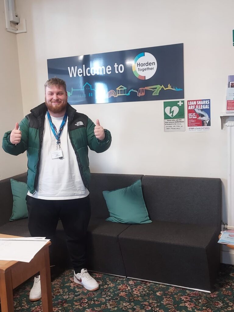 Daniel giving a double thumbs up in front of a sign for that reads 'Welcome to Horden Together'