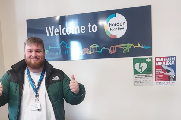 Daniel giving a double thumbs up in front of a sign that reads 'Welcome to Horden Together'